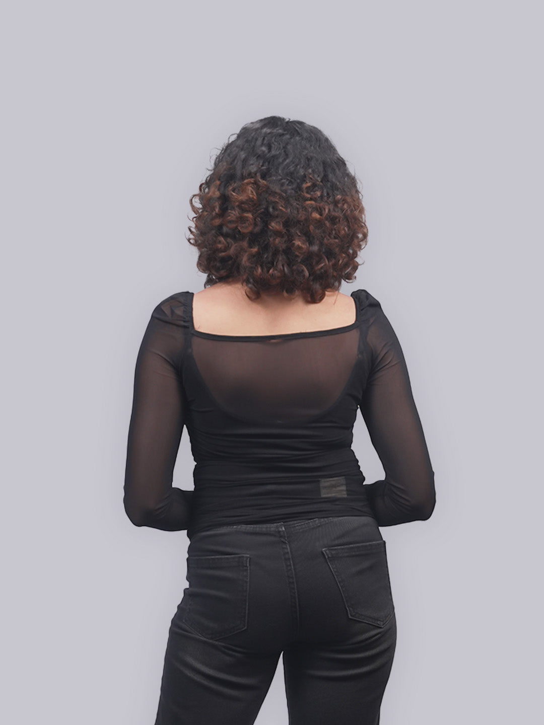 A woman viewed from behind wearing a black sheer long-sleeve top.