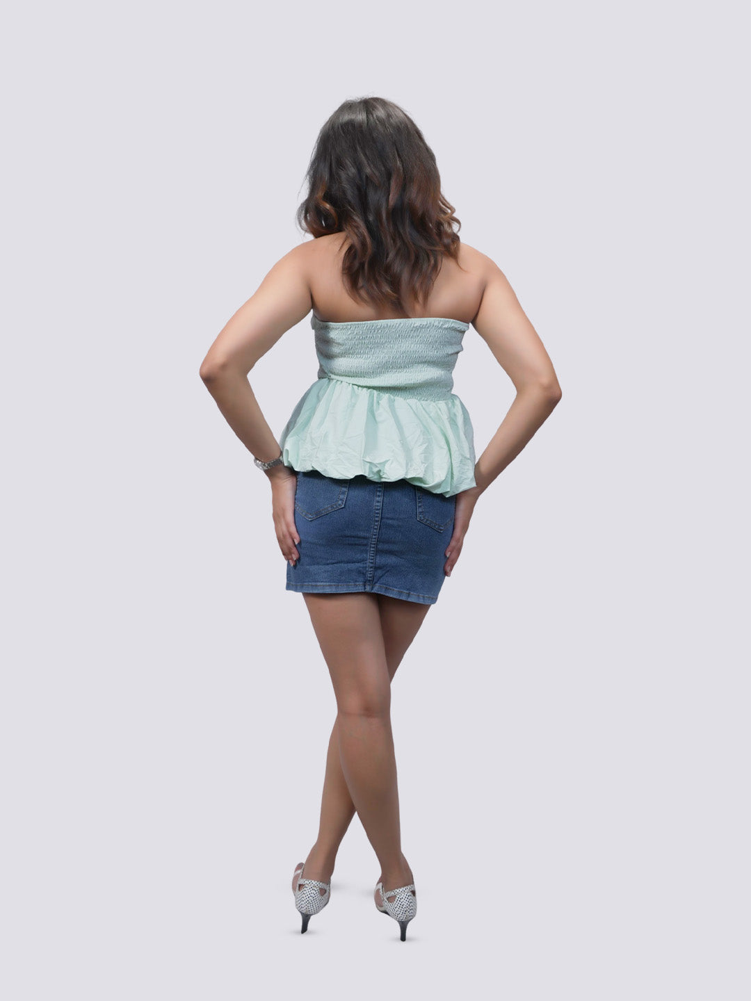 A woman is shown from behind wearing a light mint green strapless peplum top 