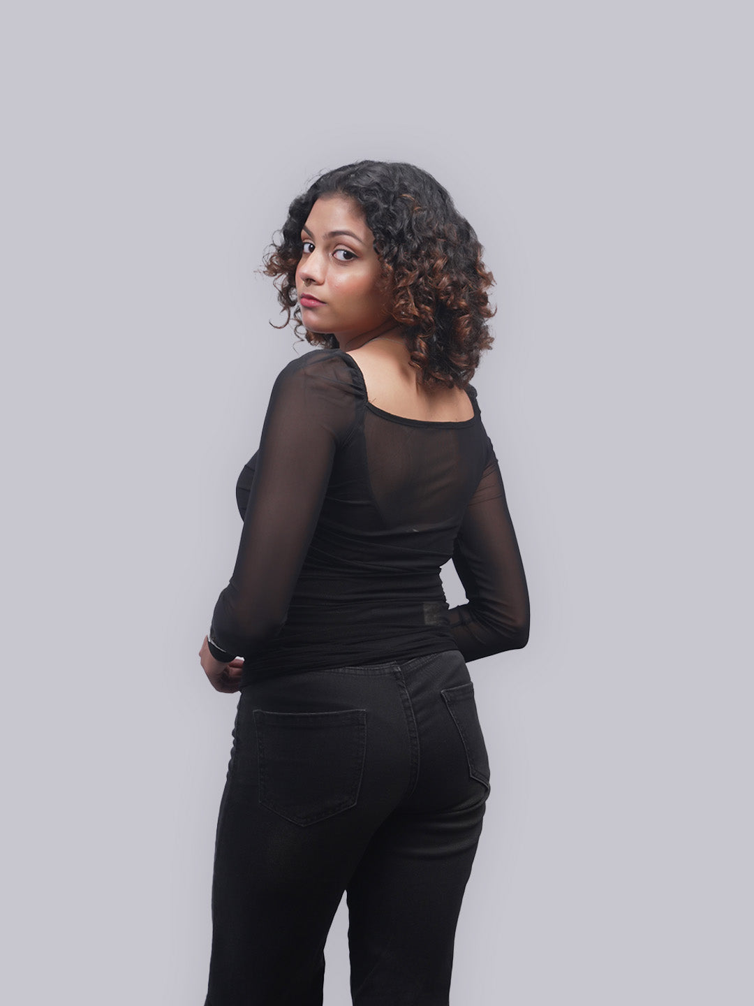 A side-back angle wearing a black sheer long-sleeve top.