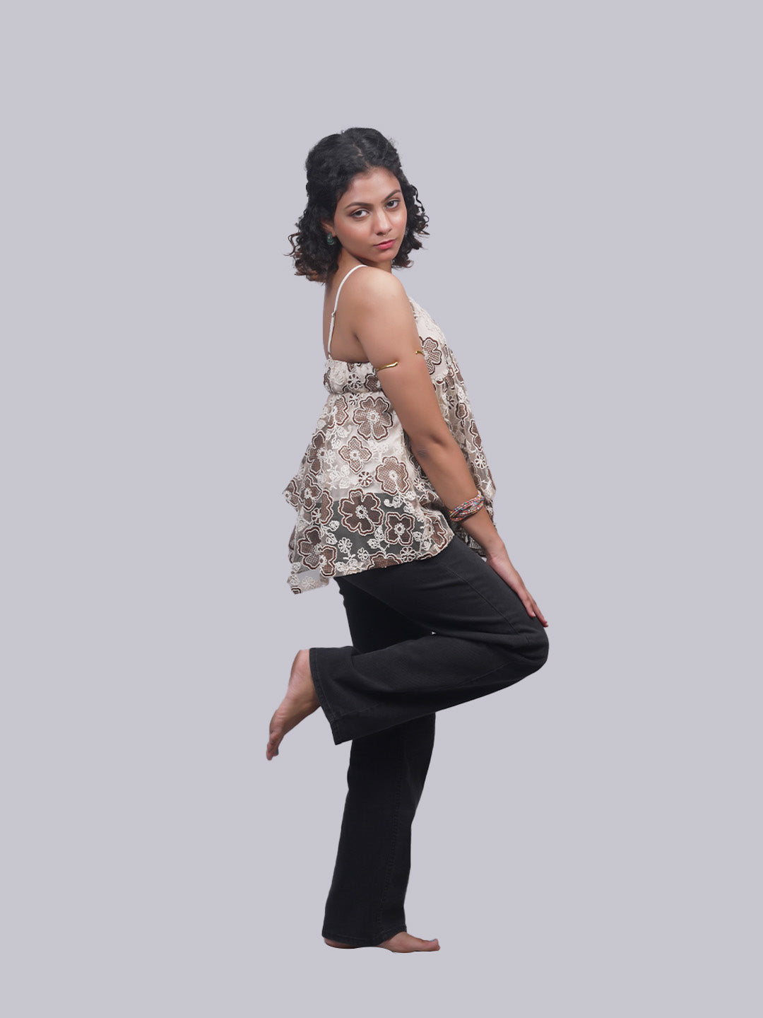 A woman posing in a sleeveless beige and brown floral print top.