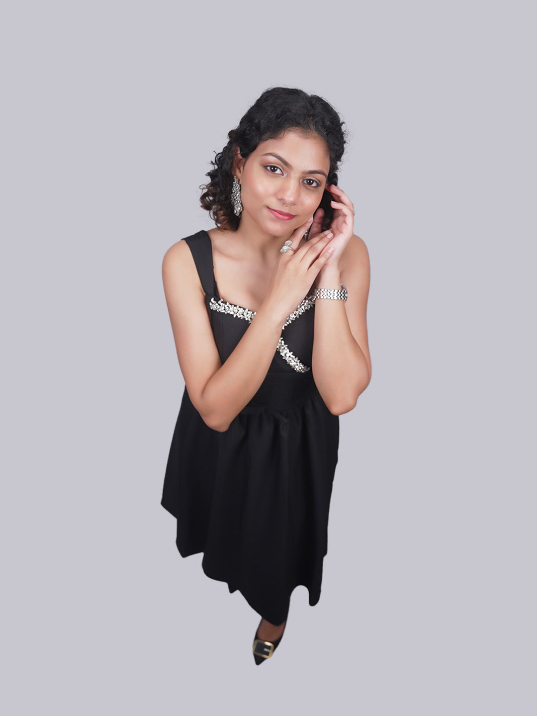 A sleeveless black dress with silver embellished trim at the neckline, posed.