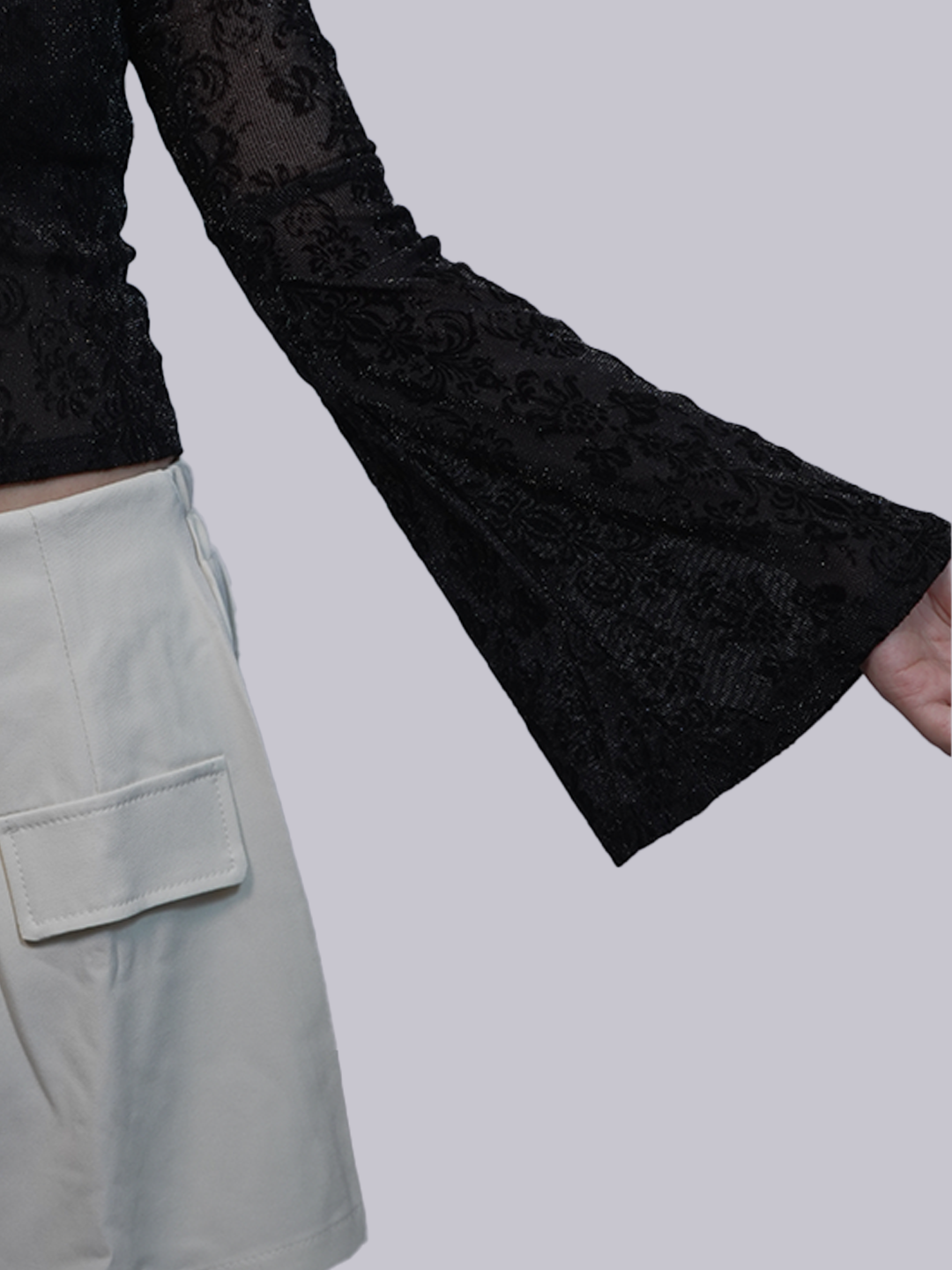 Close-up of a person wearing a black lace long-sleeve top with a flared bell sleeve.