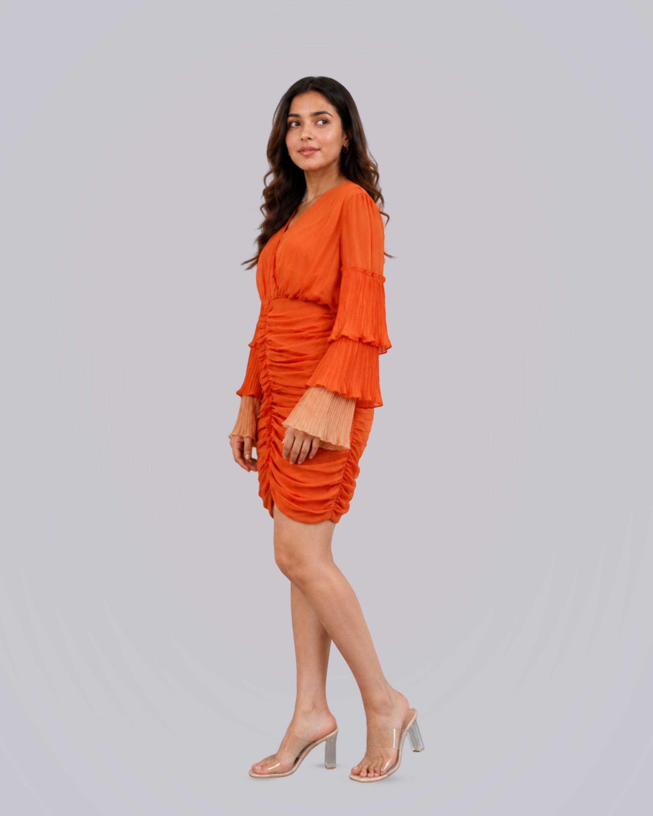 A woman modeling a bright orange ruched mini dress.
