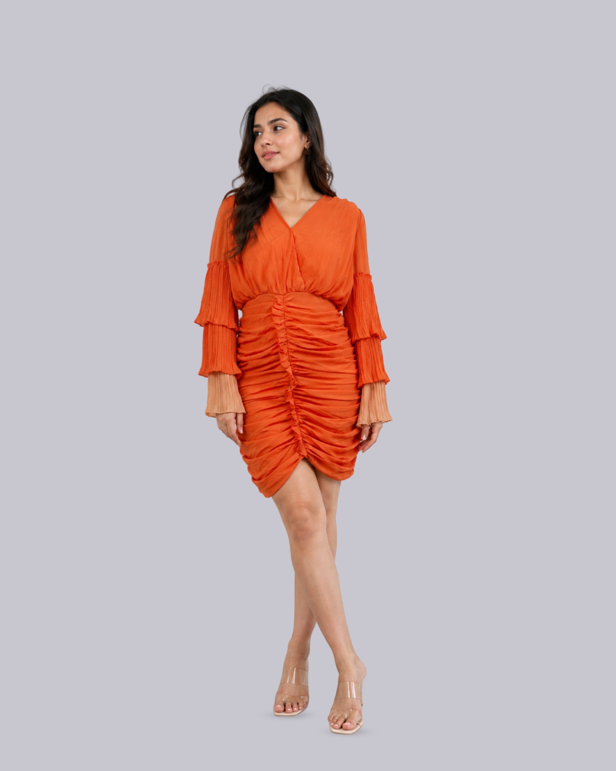 A woman modeling a bright orange ruched mini dress.