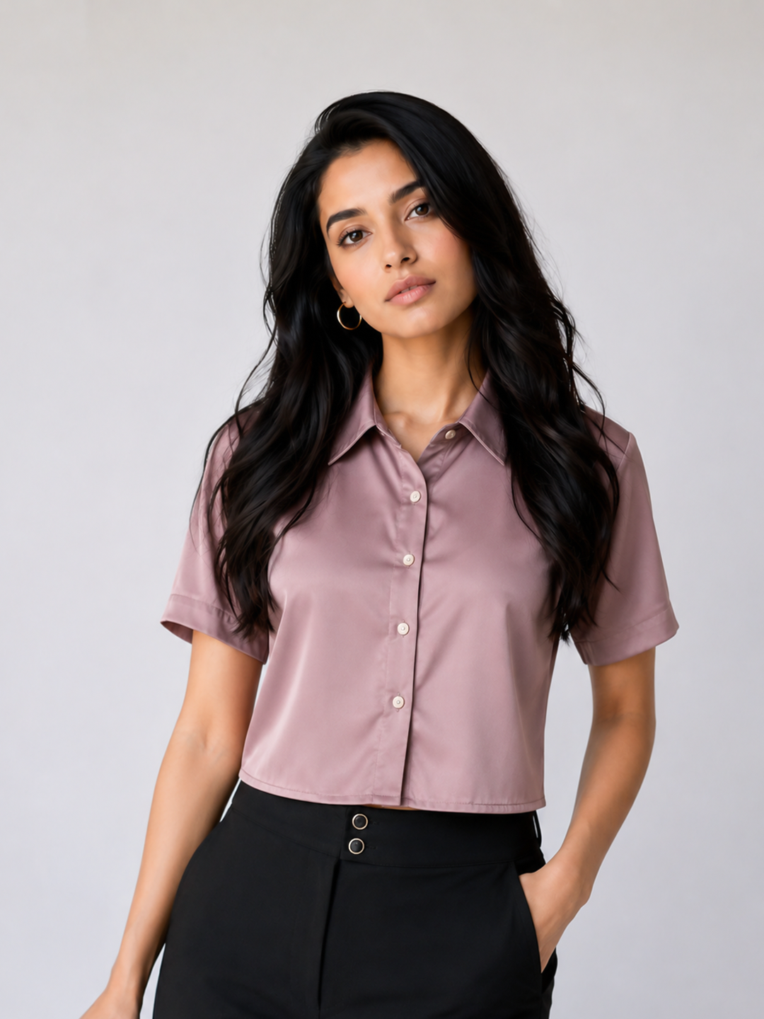 A woman modeling a short-sleeve button-up shirt in a dusty mauve color, paired with black pants.