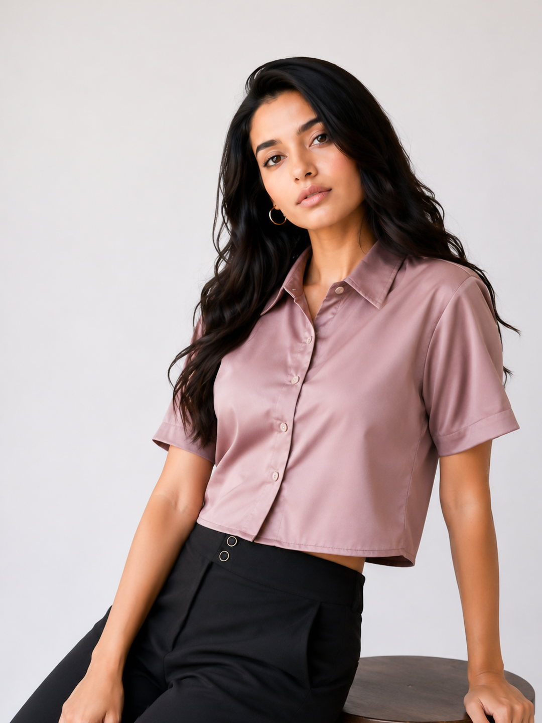 A woman wearing a short-sleeve, button-up satin blouse in a dusty mauve pink color.