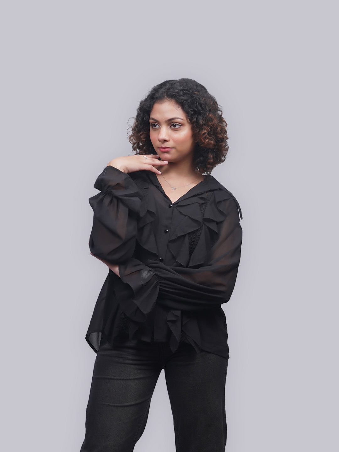 A woman with curly dark hair wearing a black sheer long-sleeve top.