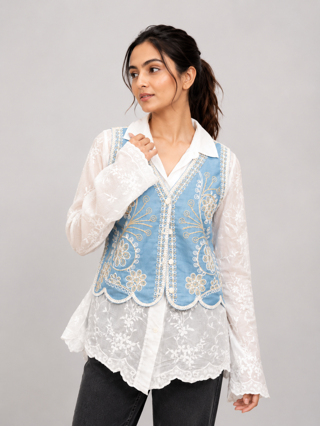 A light blue embroidered vest over a white lace blouse, paired with black pants