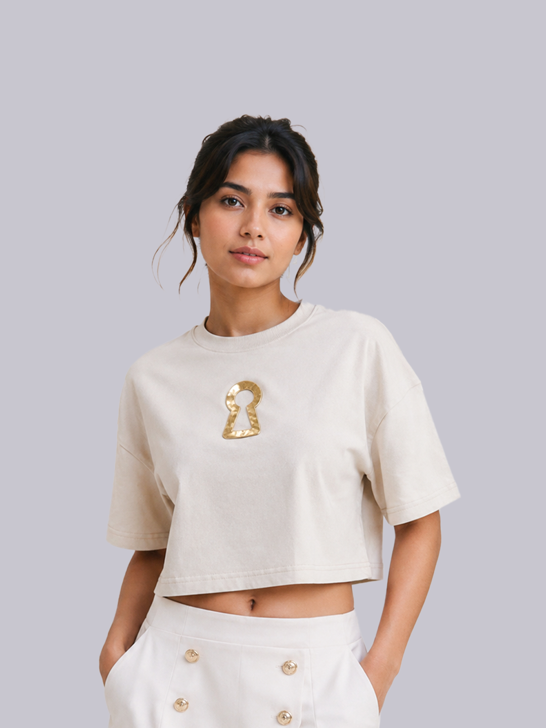 A woman modeling a cropped off-white t-shirt with a metallic gold keyhole graphic on the chest,