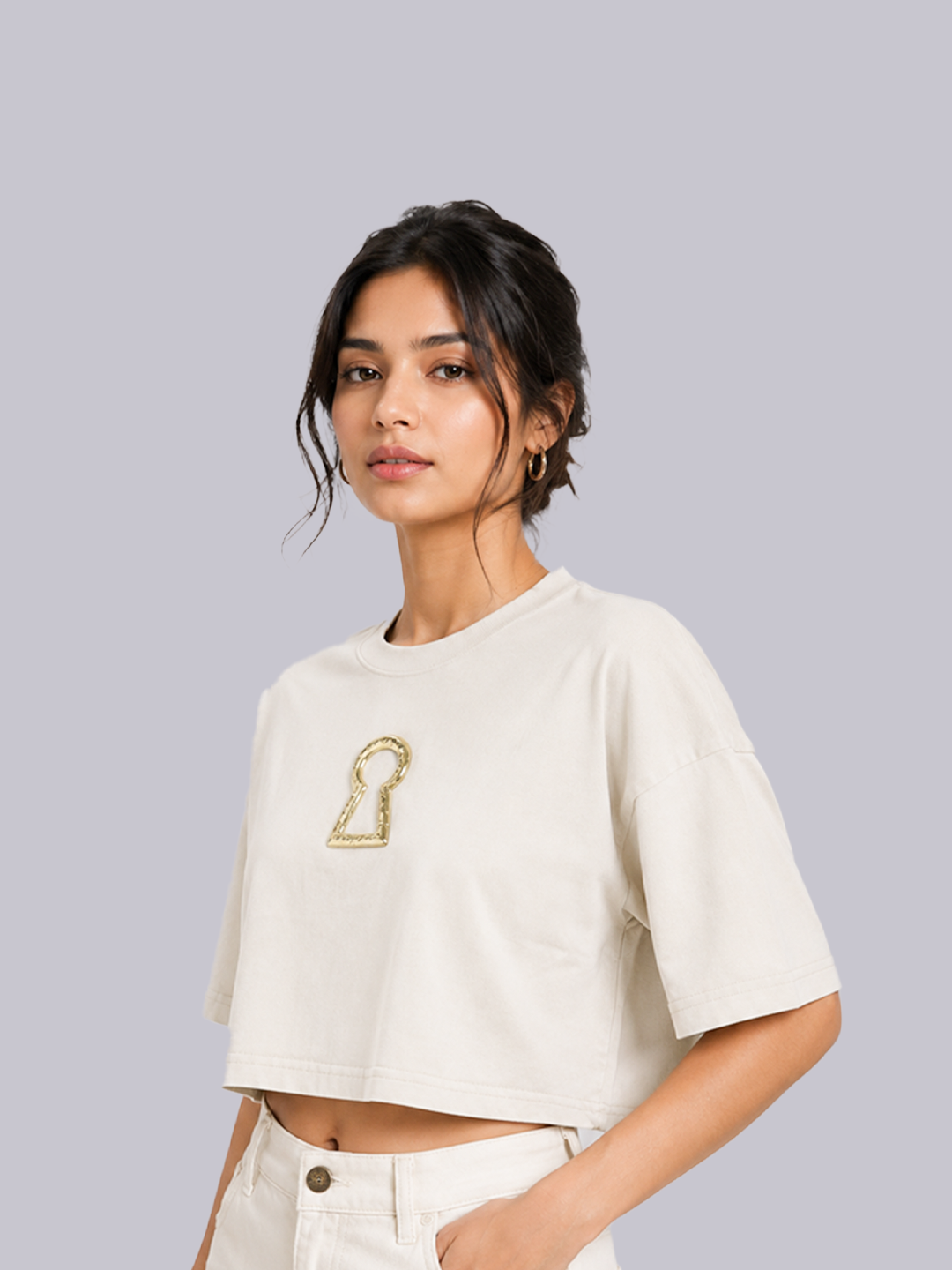 A woman modeling a cropped off-white t-shirt with a gold metallic.
